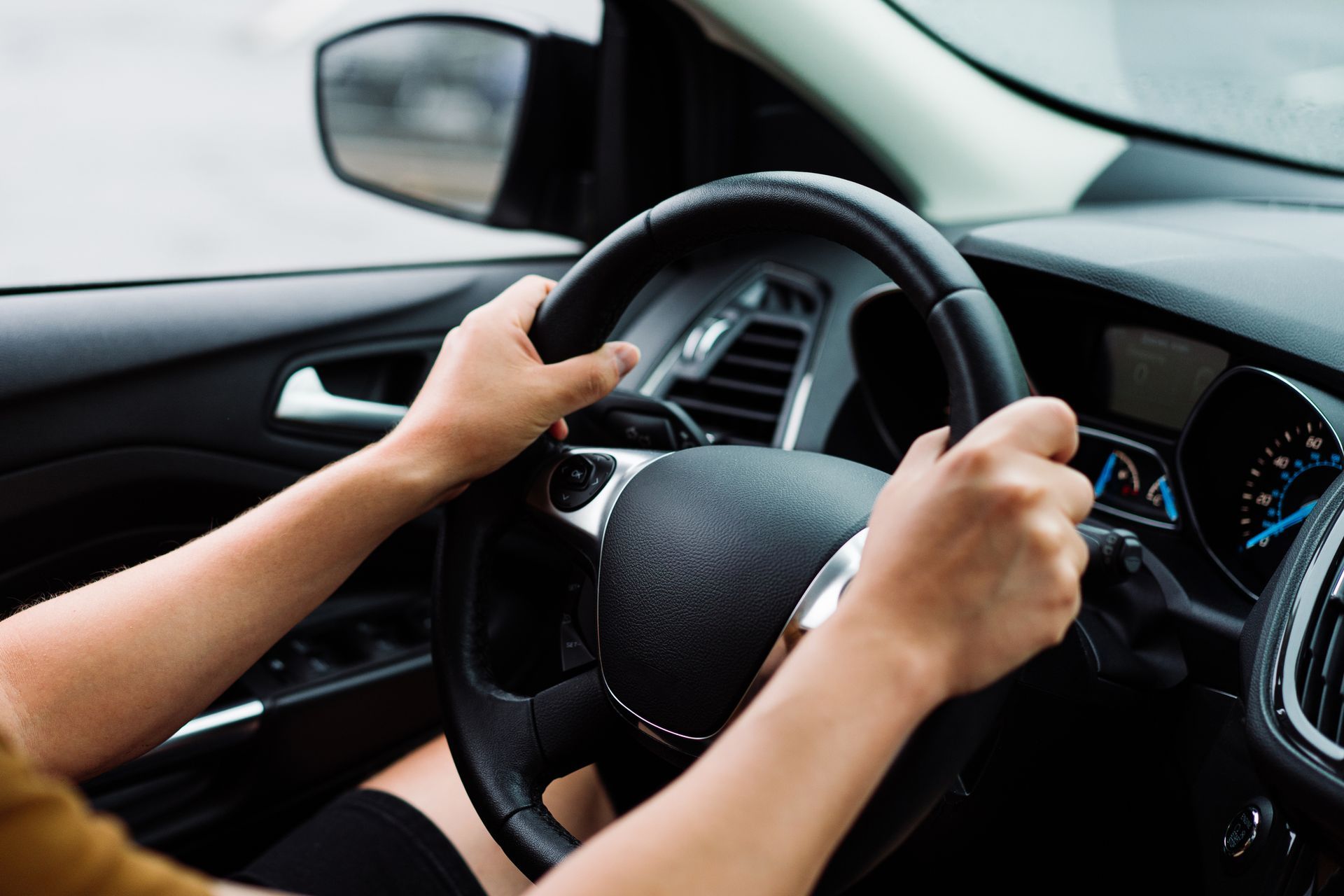 Hands gripping the steering wheel of a contemporary vehicle.