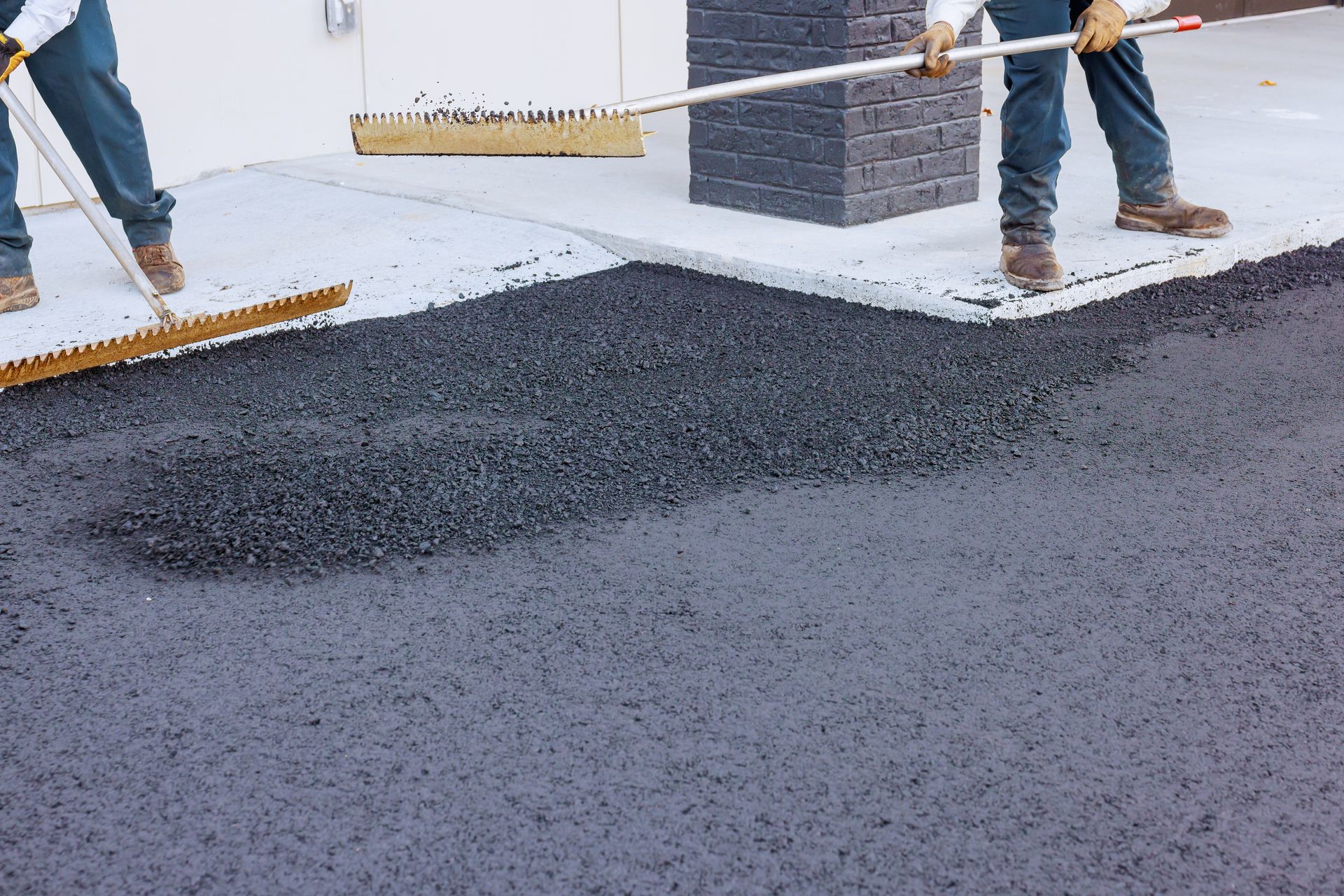 Workers spreading fresh asphalt with rakes to create a smooth surface near a concrete edge. Workers spreading fresh asphalt with rakes to create a smooth surface near a concrete edge.