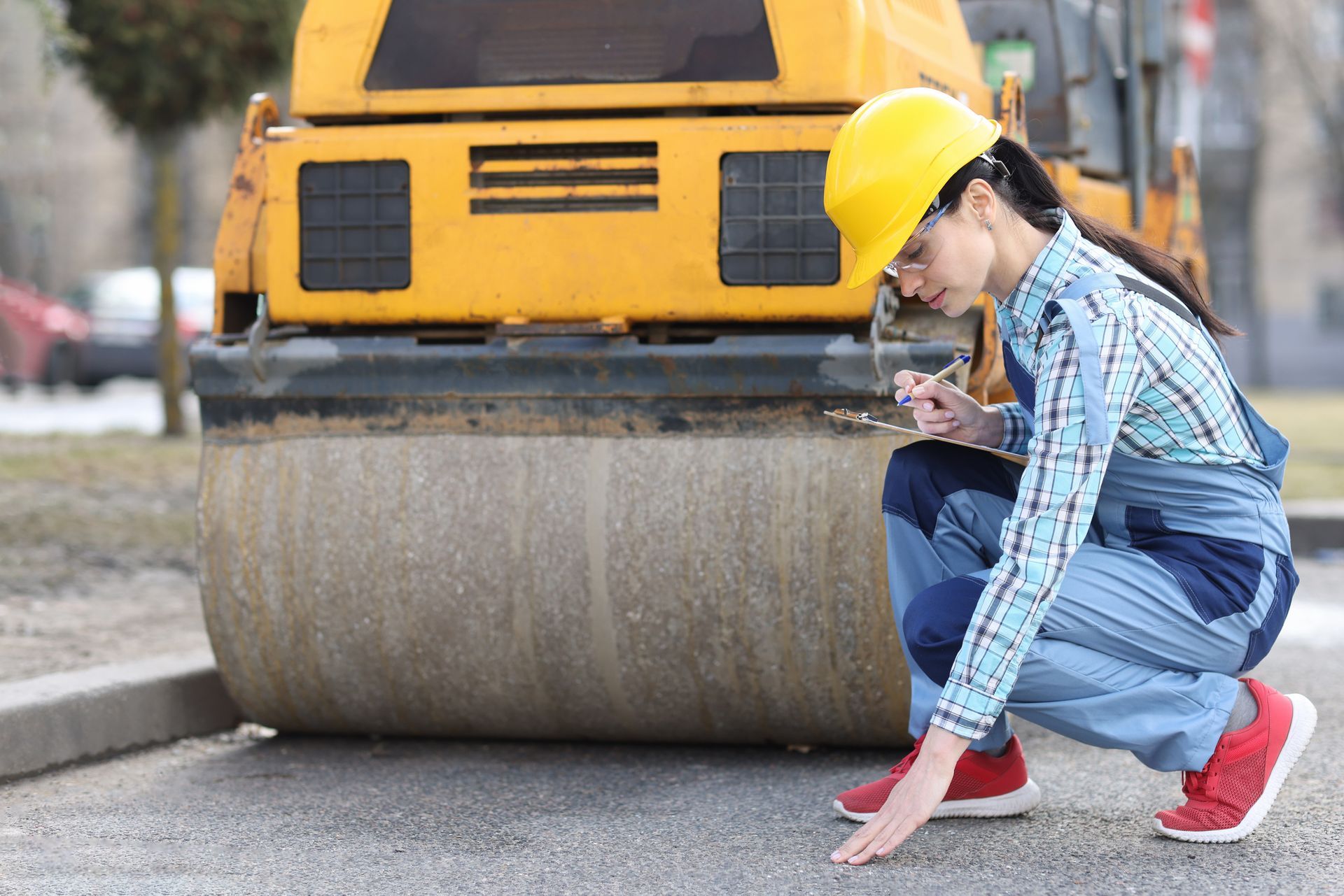 Woman examines asphalt pavement in front of asphalt paver.