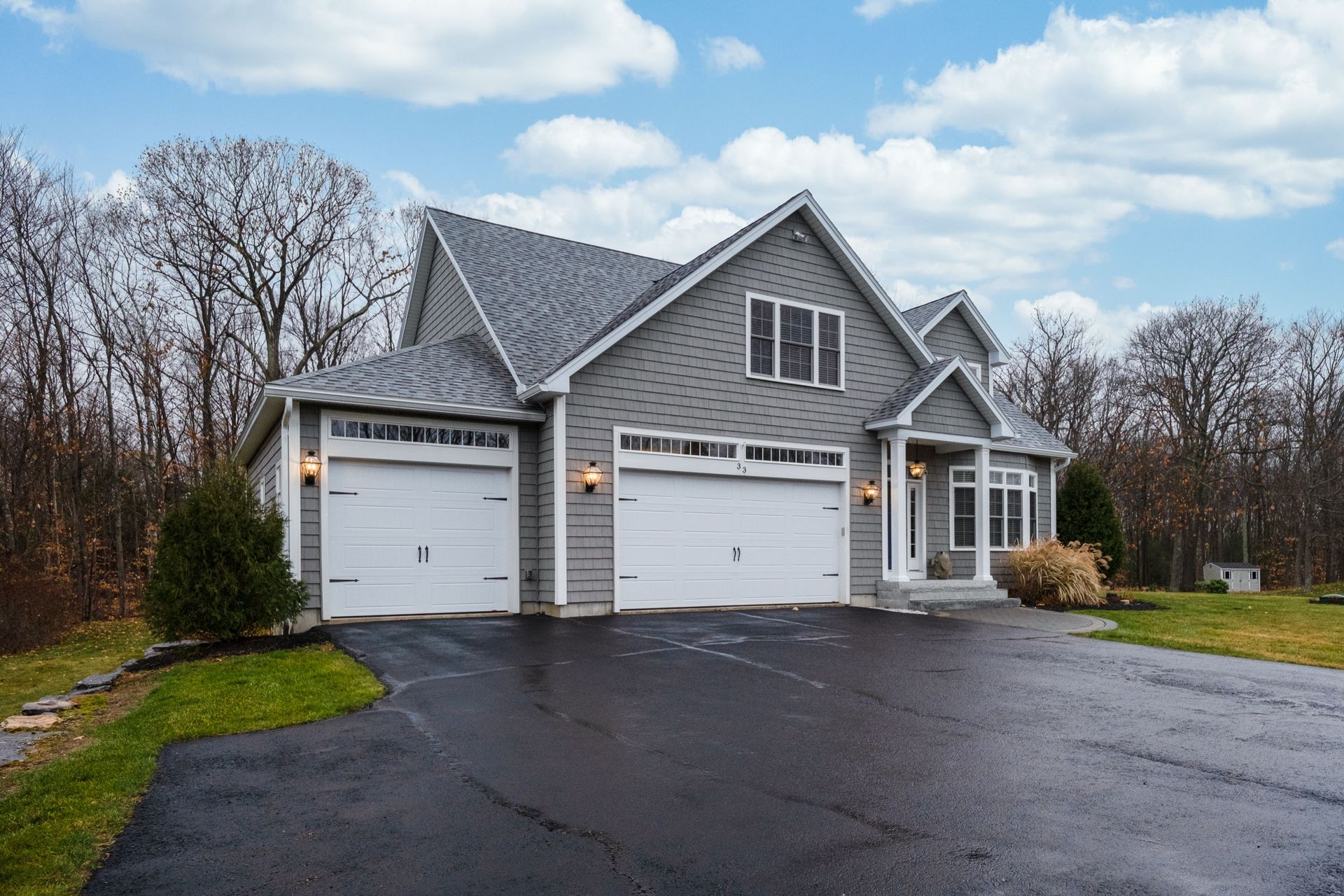 Gray suburban home with white trim, wet black driveway, and three-car garage. Gray suburban home with white trim, wet black driveway, and three-car garage.