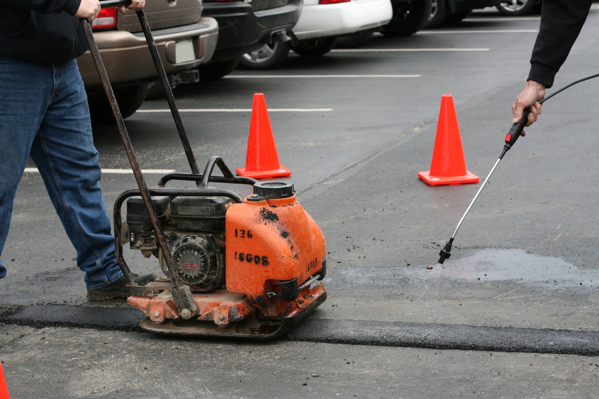 Cropped view of a worker performing asphalt maintenance by doing patch repair on a parking lot.