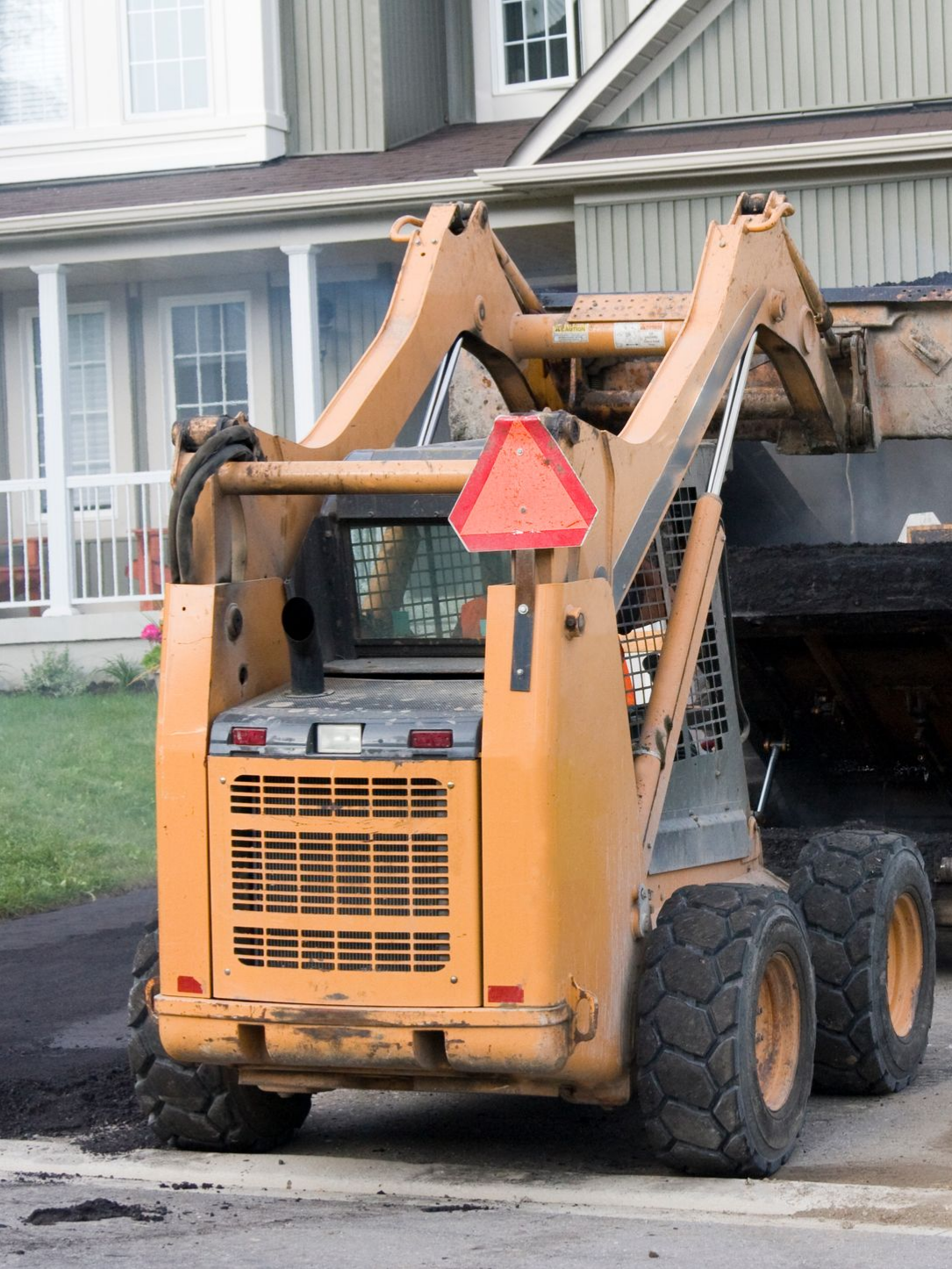 Driveway asphalt contractors operating a paving machine to lay asphalt on a residential driveway. Driveway asphalt contractors operating a paving machine to lay asphalt on a residential driveway.