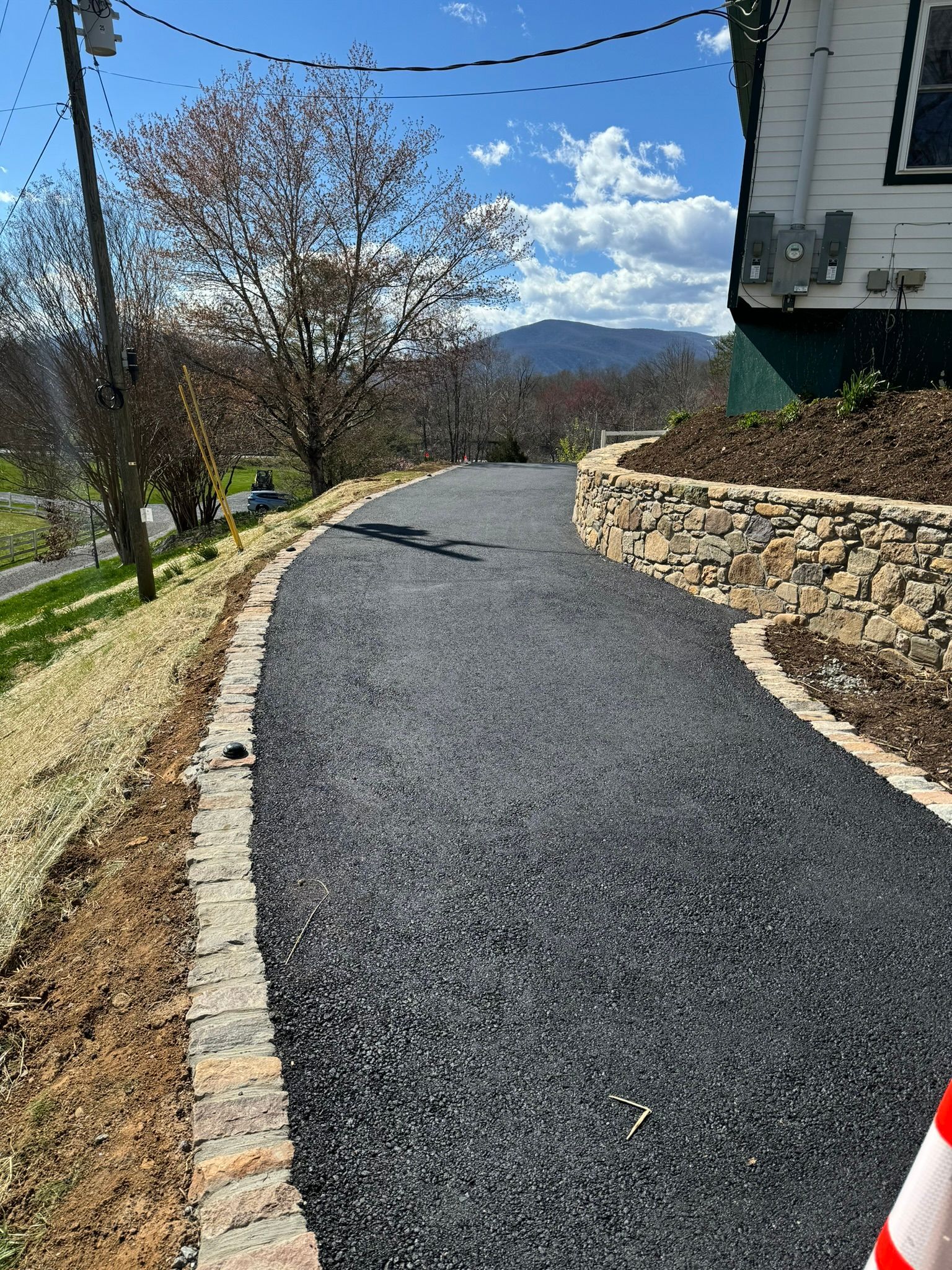 A road with a stone wall on the side of it and a house in the background.