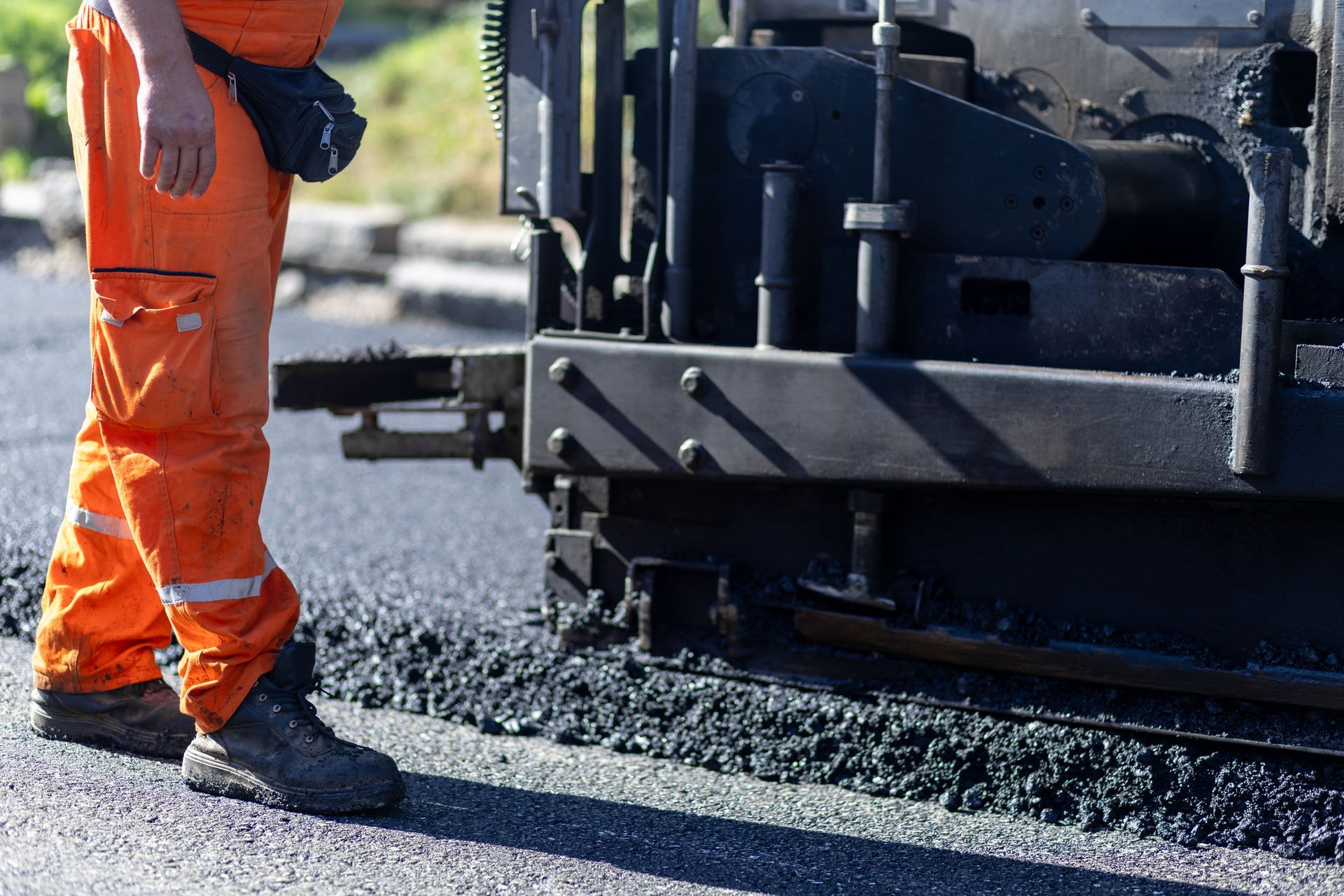 Worker operating asphalt paver during daytime on a new roadway project.