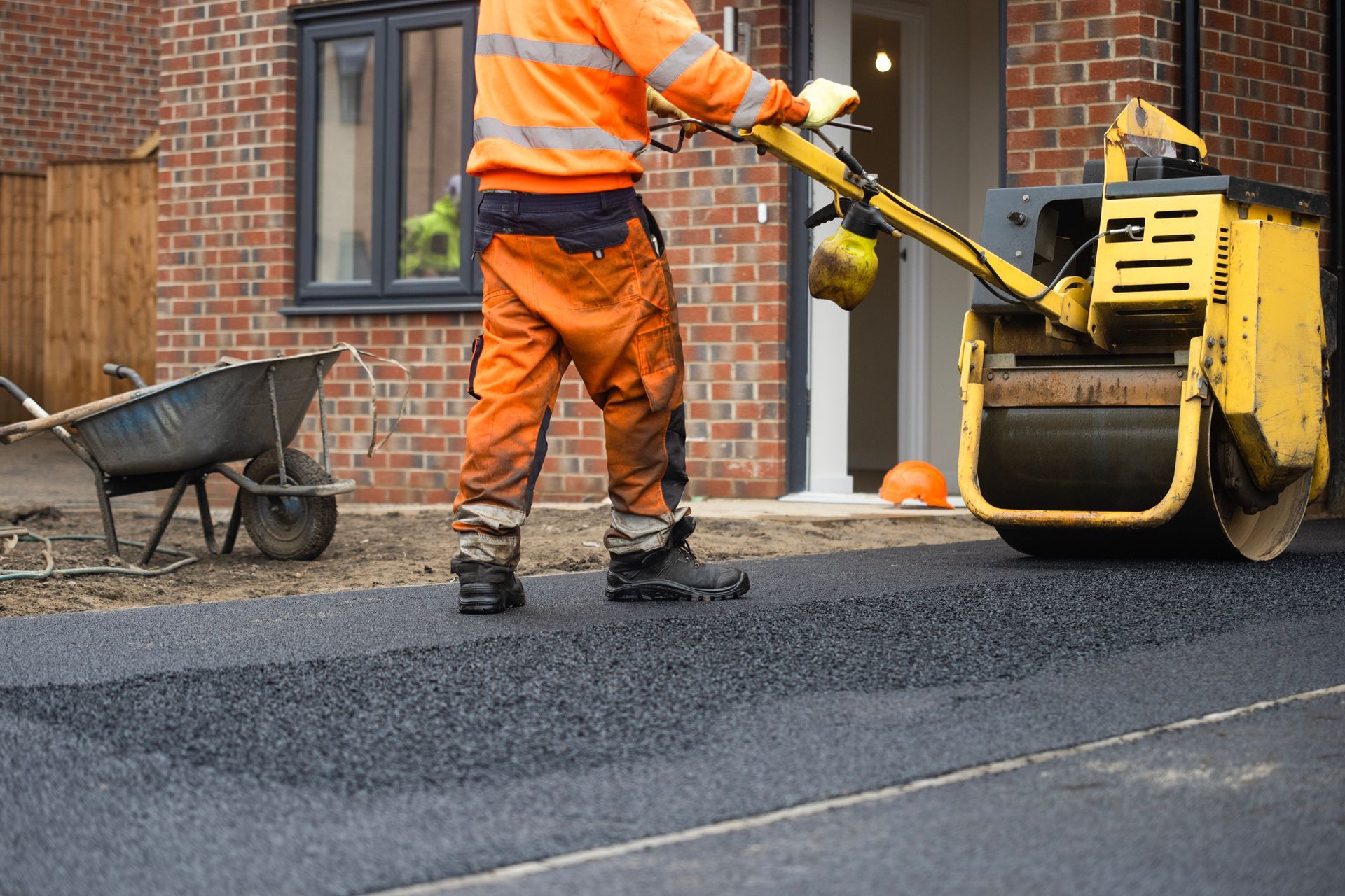 Driveway paving contractor operating asphalt roller to smooth freshly laid pavement.