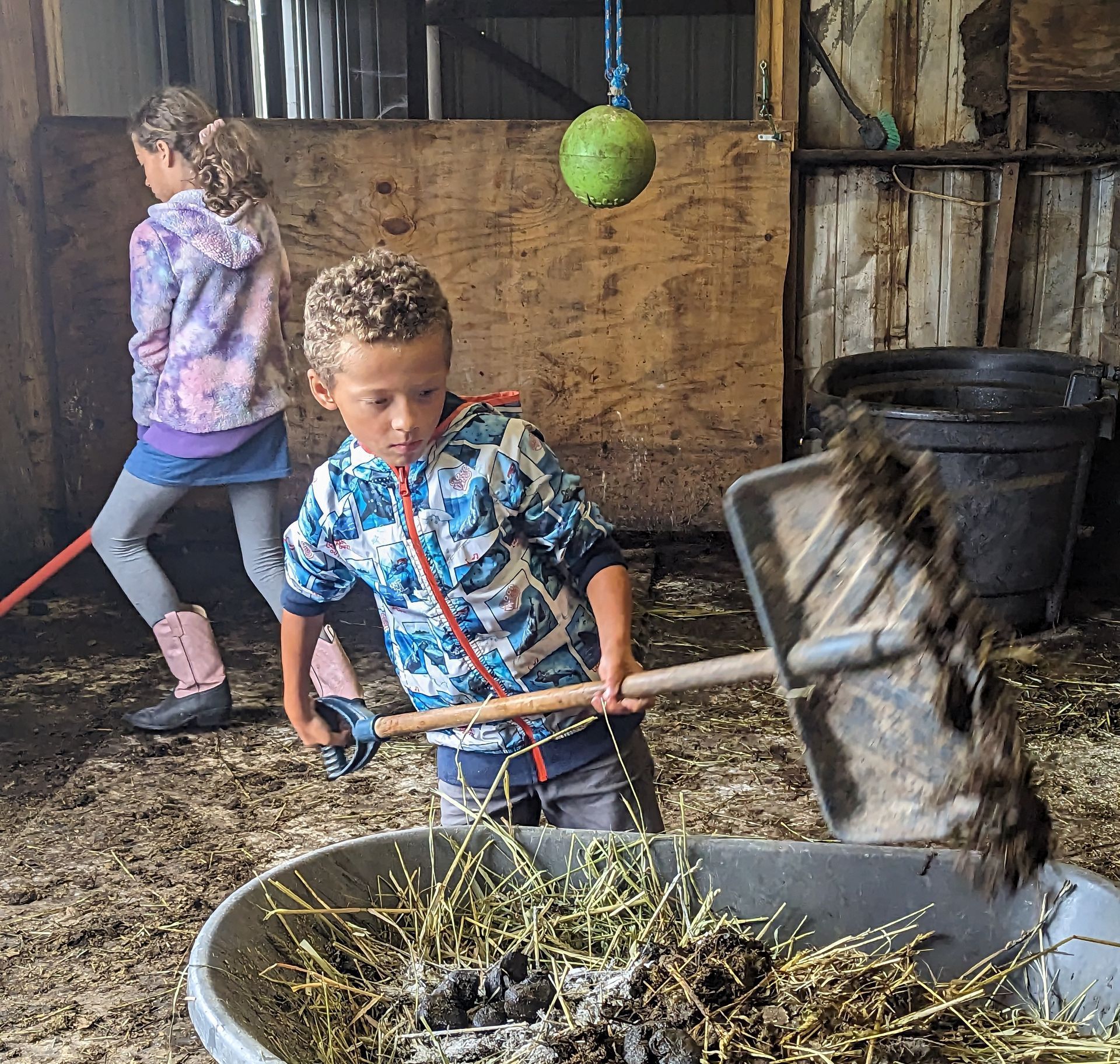 a boy is holding a shovel over a bucket of hay/manure