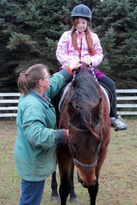 A woman is petting a young girl on a horse.