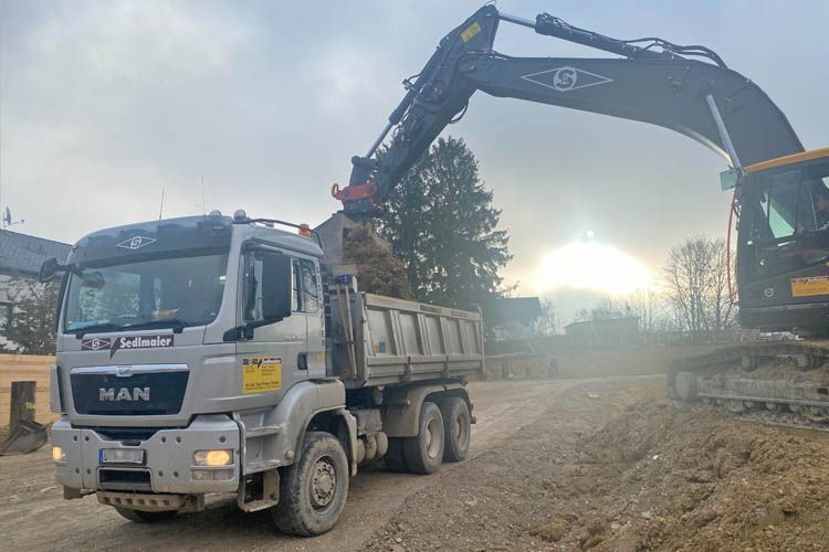 Ein Muldenkipper wird von einem Bagger mit Erde beladen.