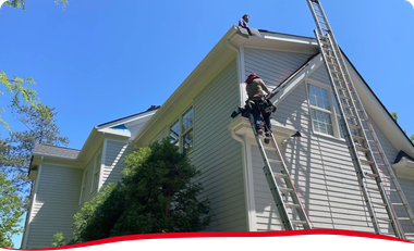 A man on a ladder is working on the roof of a house