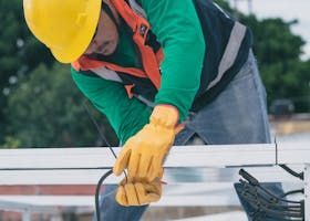 Two workers on a house roof and ladder, working on a gutter installation.
