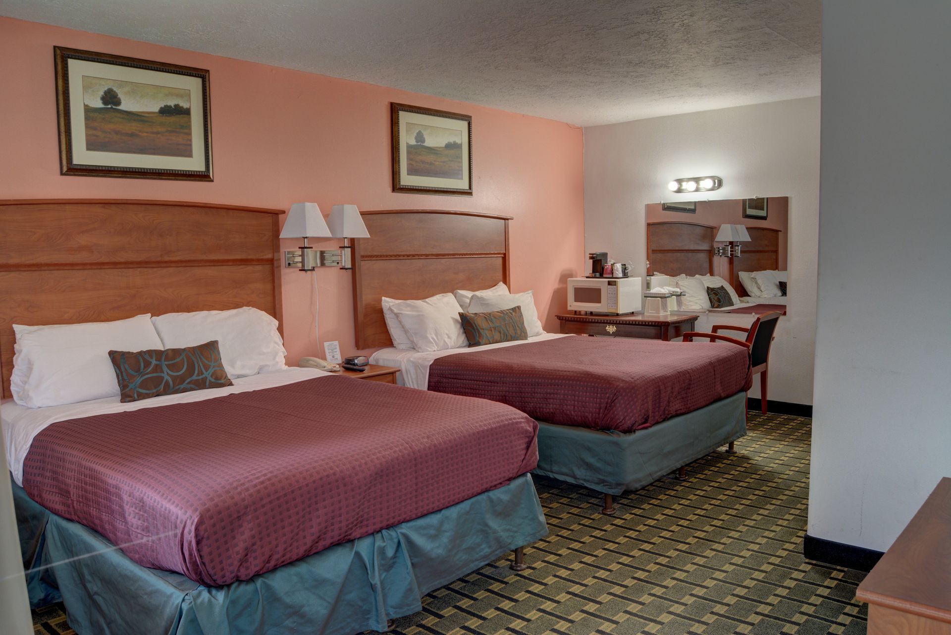 Two double beds in a motel room with burgundy bedspreads, pink walls, and a desk area.