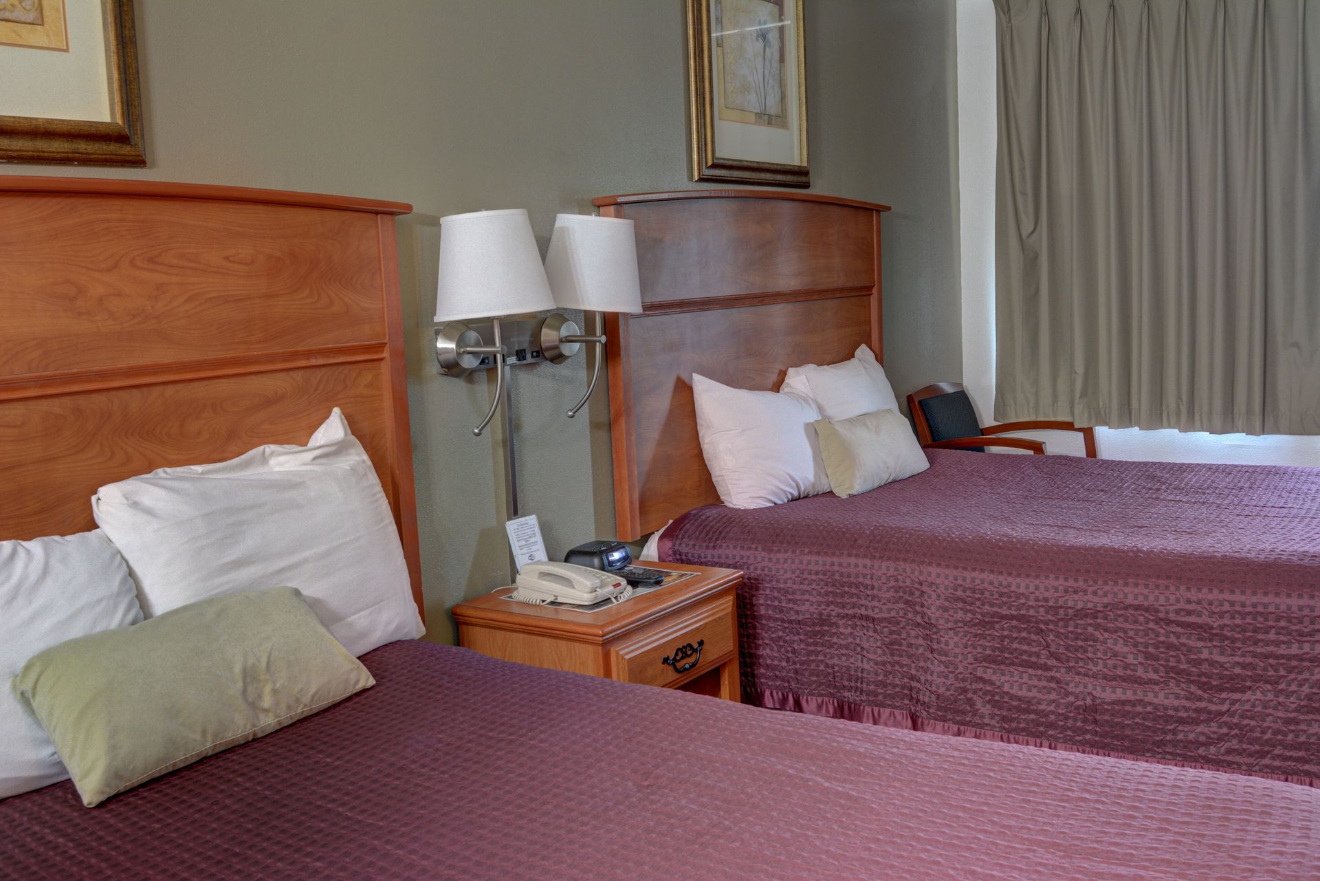 A hotel room with two beds, each with white pillows and a plum-colored bedspread.