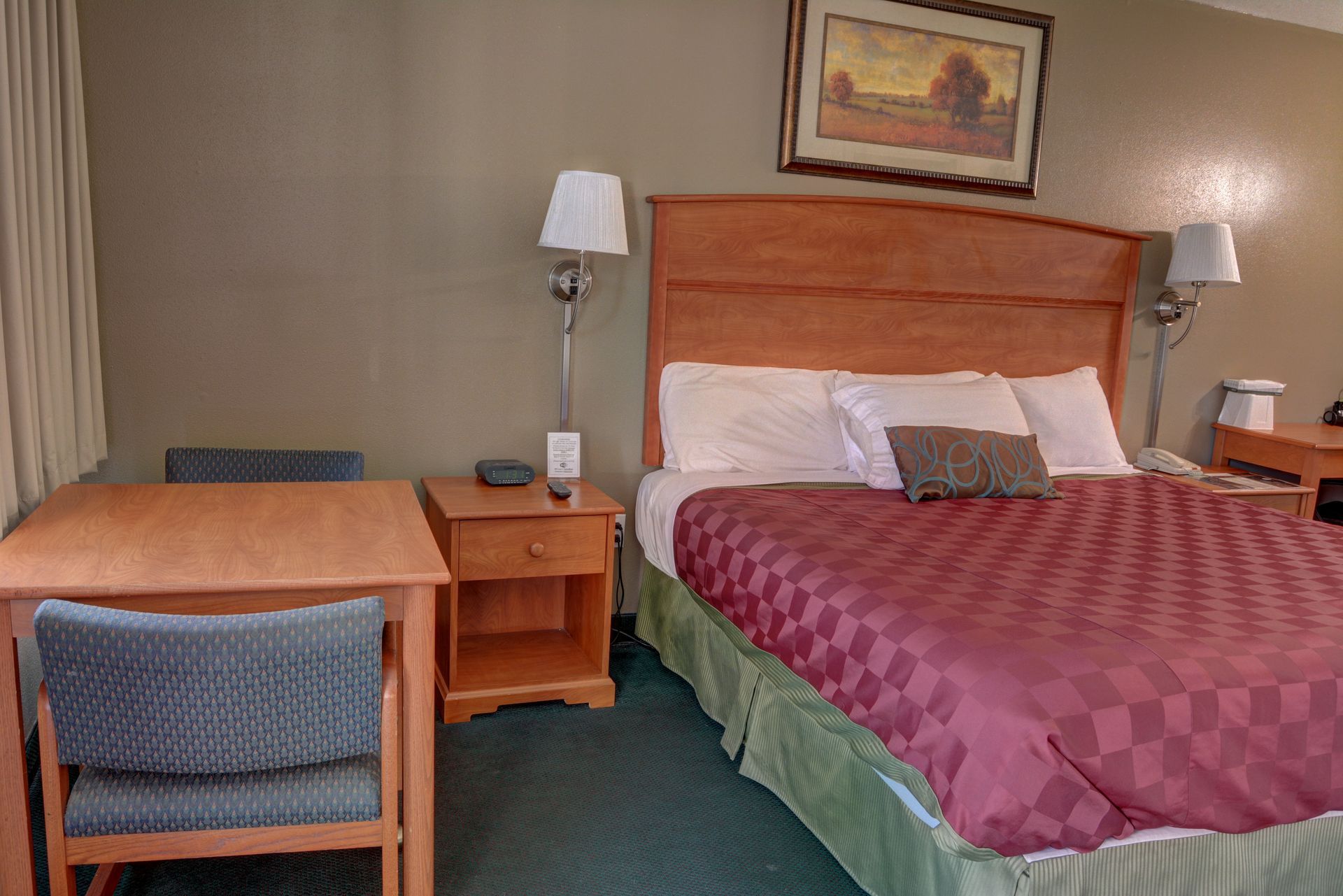 A hotel room with a bed, desk, and nightstand. The bed has a red patterned comforter.