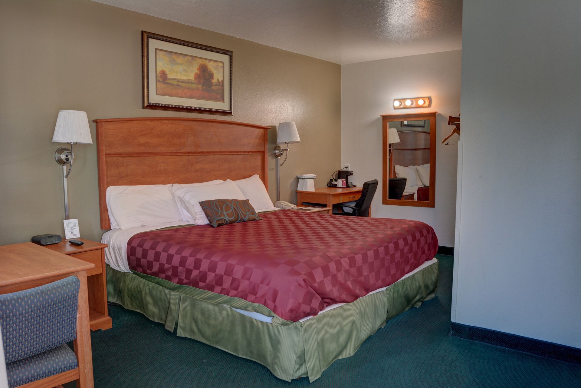 Bedroom with a king-sized bed, desk, and lamps. The bed has a maroon comforter and the walls are light brown.