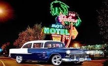 Blue and white classic car with flame decals parked in front of a lit 