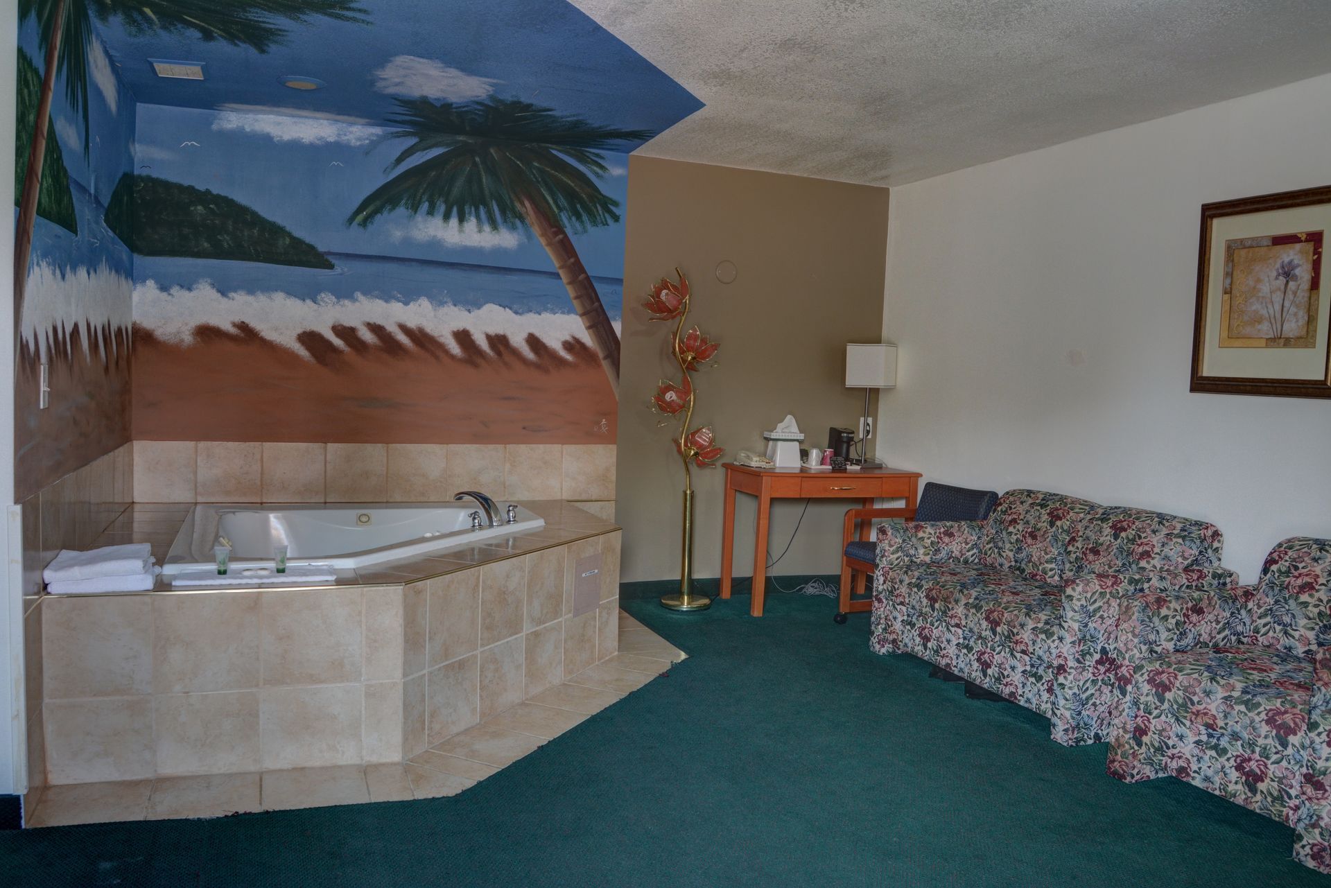 Hotel room with a jacuzzi, a painted mural of a beach scene, a small table, and patterned couch.