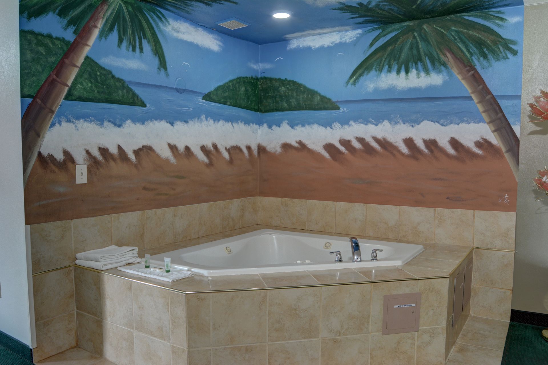 A jacuzzi tub in a corner, with a painted beach scene on the surrounding walls. Palm trees