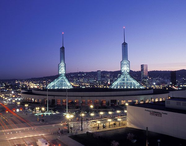 Portland, Oregon Convention Center at dusk, with two tall spires illuminated, overlooking city lights and a busy street.