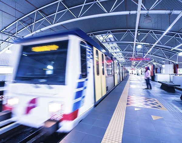 A speeding train pulling into a subway station. A person stands on the platform, waiting.