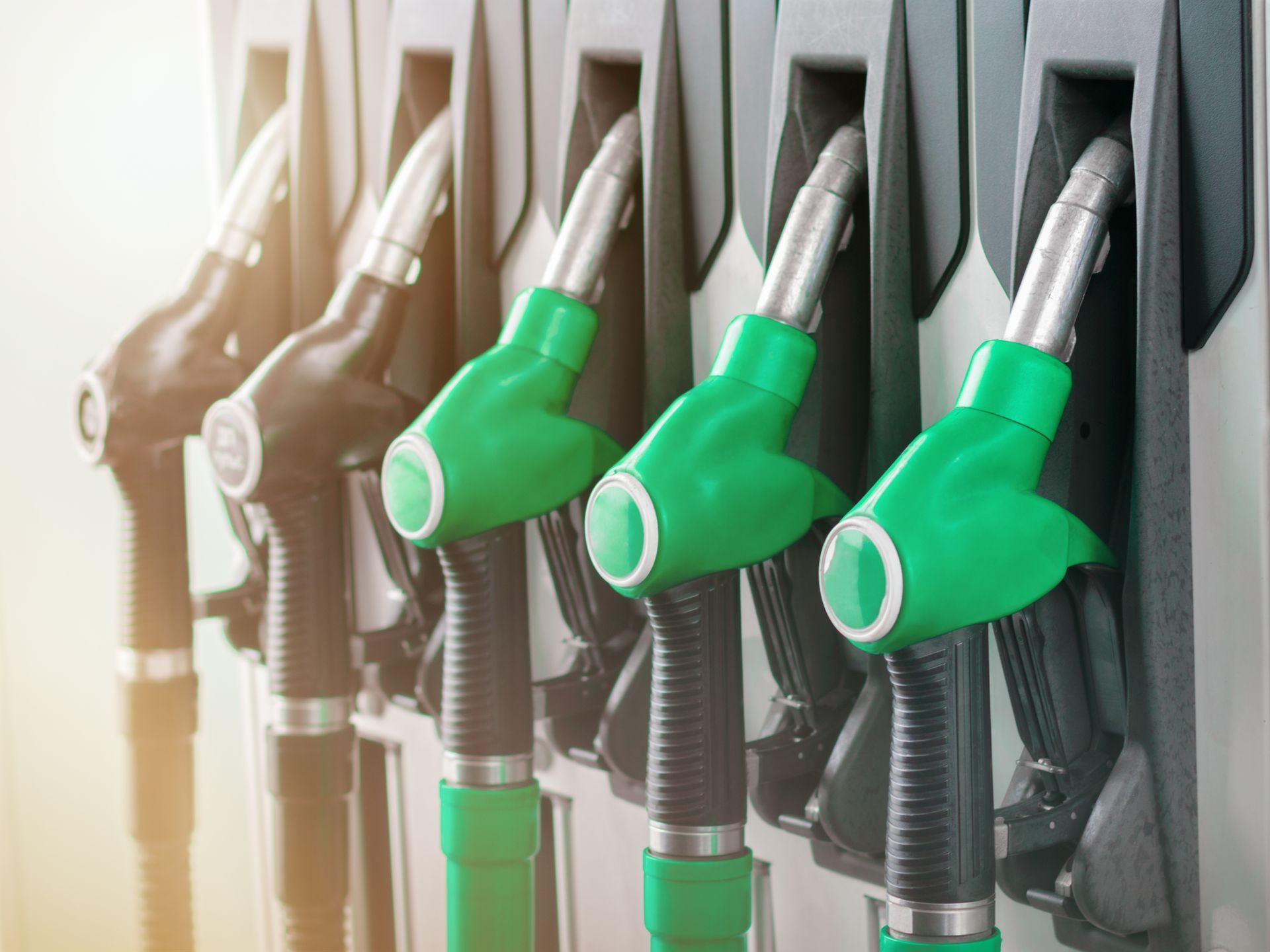 Fuel pump nozzles, with green handles, lined up at a gas station.