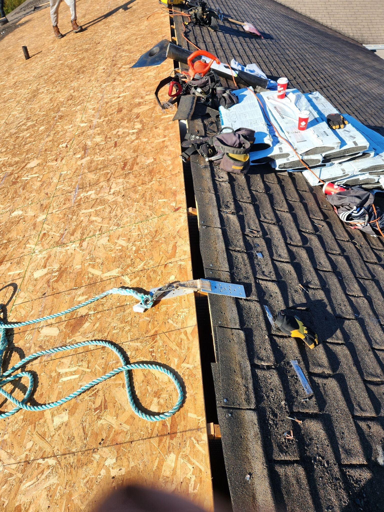 A person is working on a roof with tools and a rope.