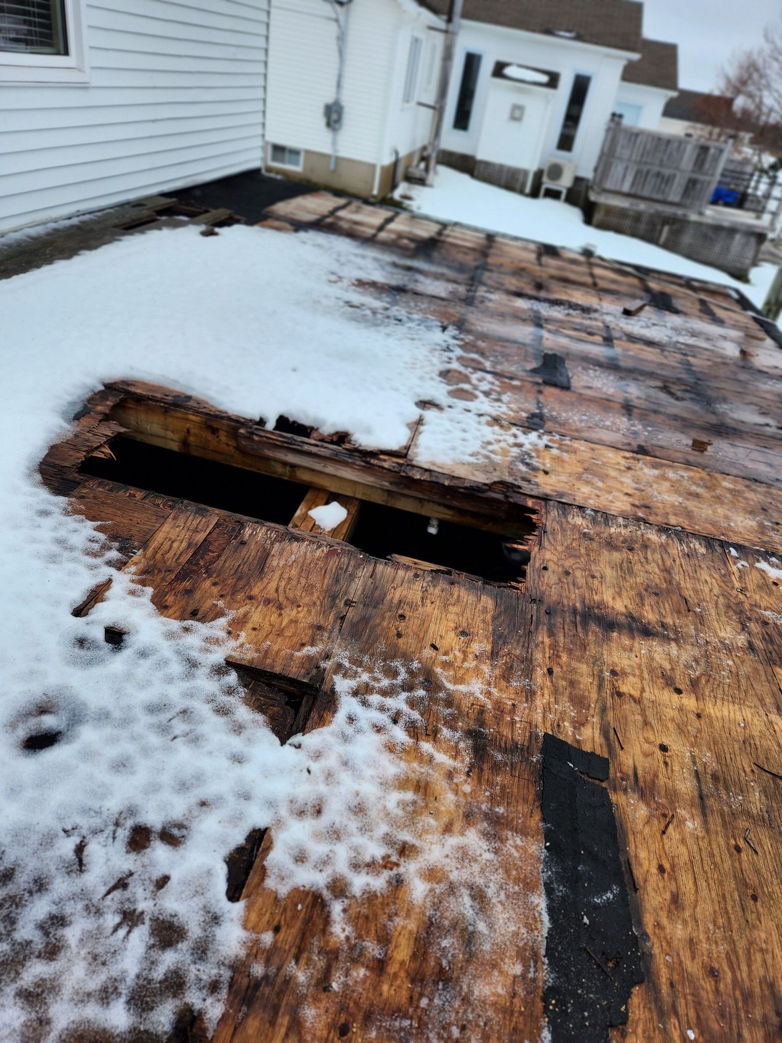 A roof with a hole in it is covered in snow.