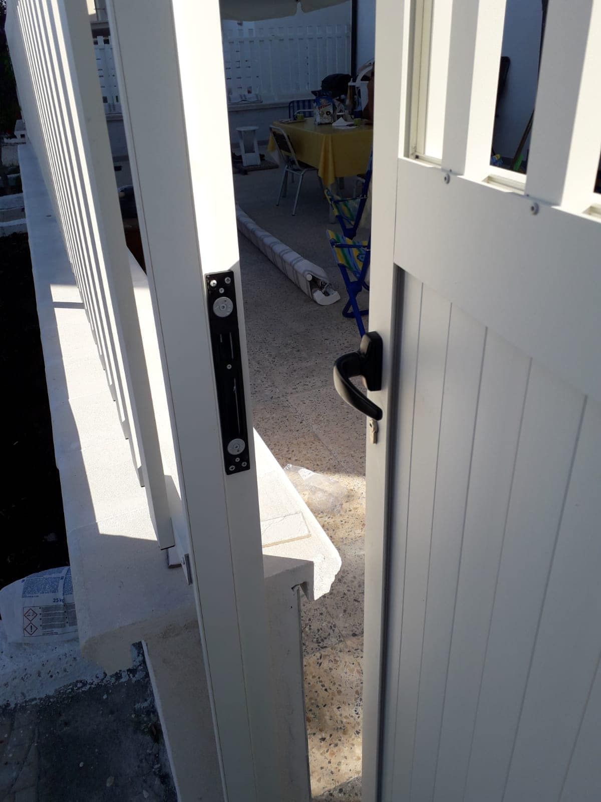 Un cancello bianco con una maniglia nera è aperto su un patio