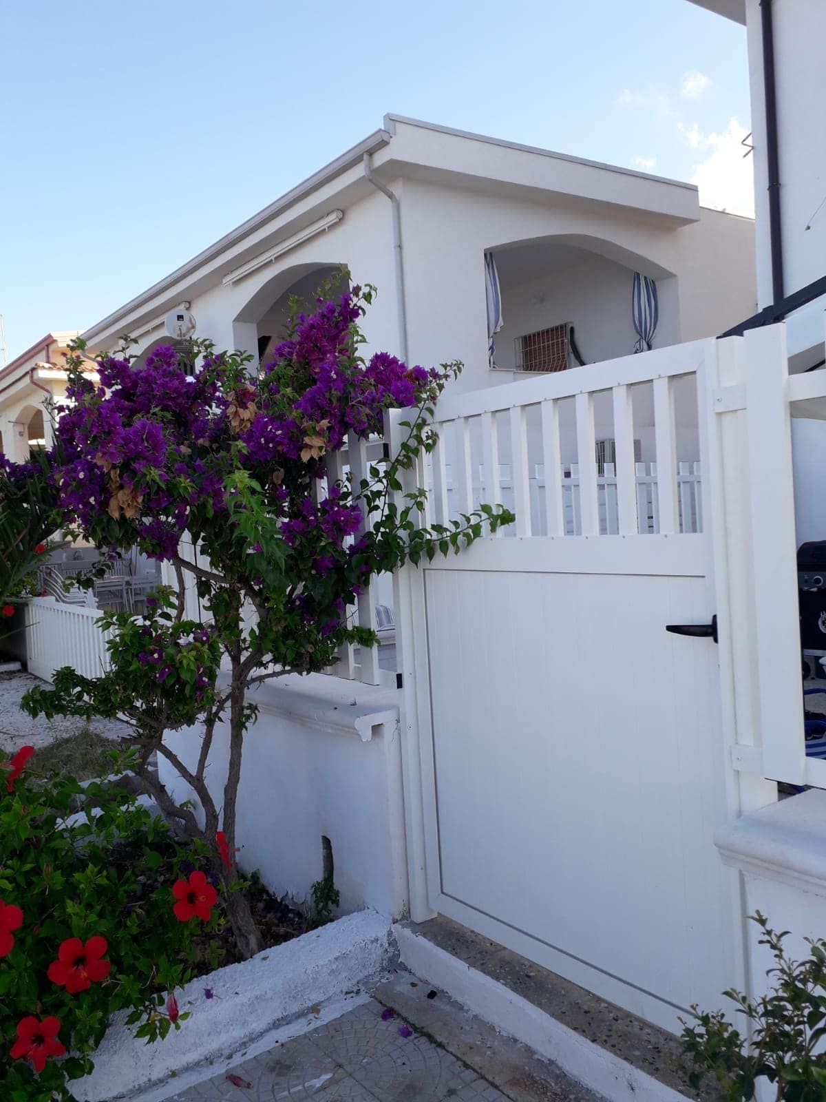 Una staccionata bianca con fiori viola davanti a una casa bianca