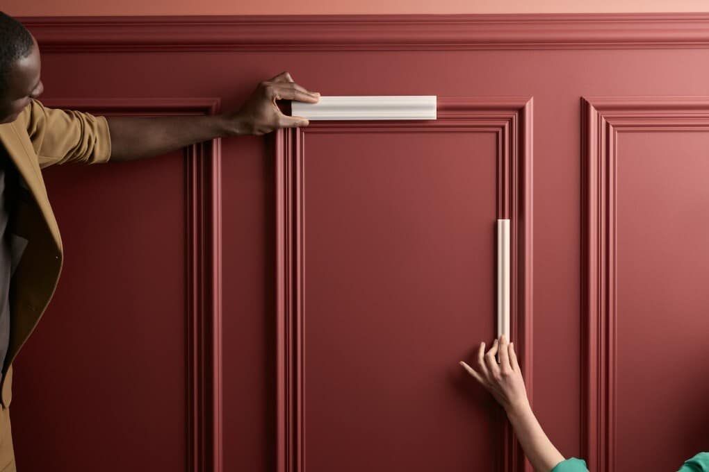 Un uomo e una donna stanno installando delle modanature su un muro rosso.