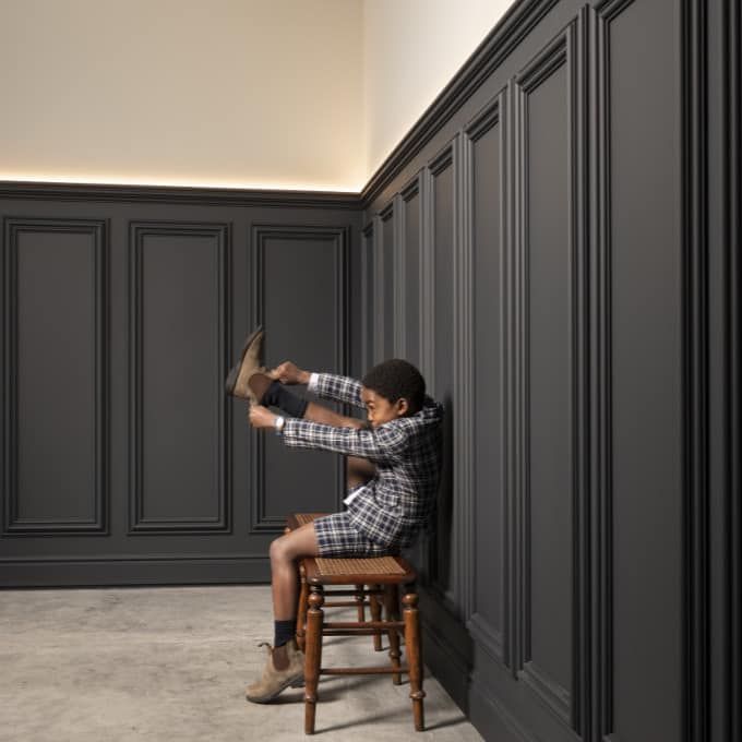 Un ragazzino è seduto su uno sgabello davanti a un muro.