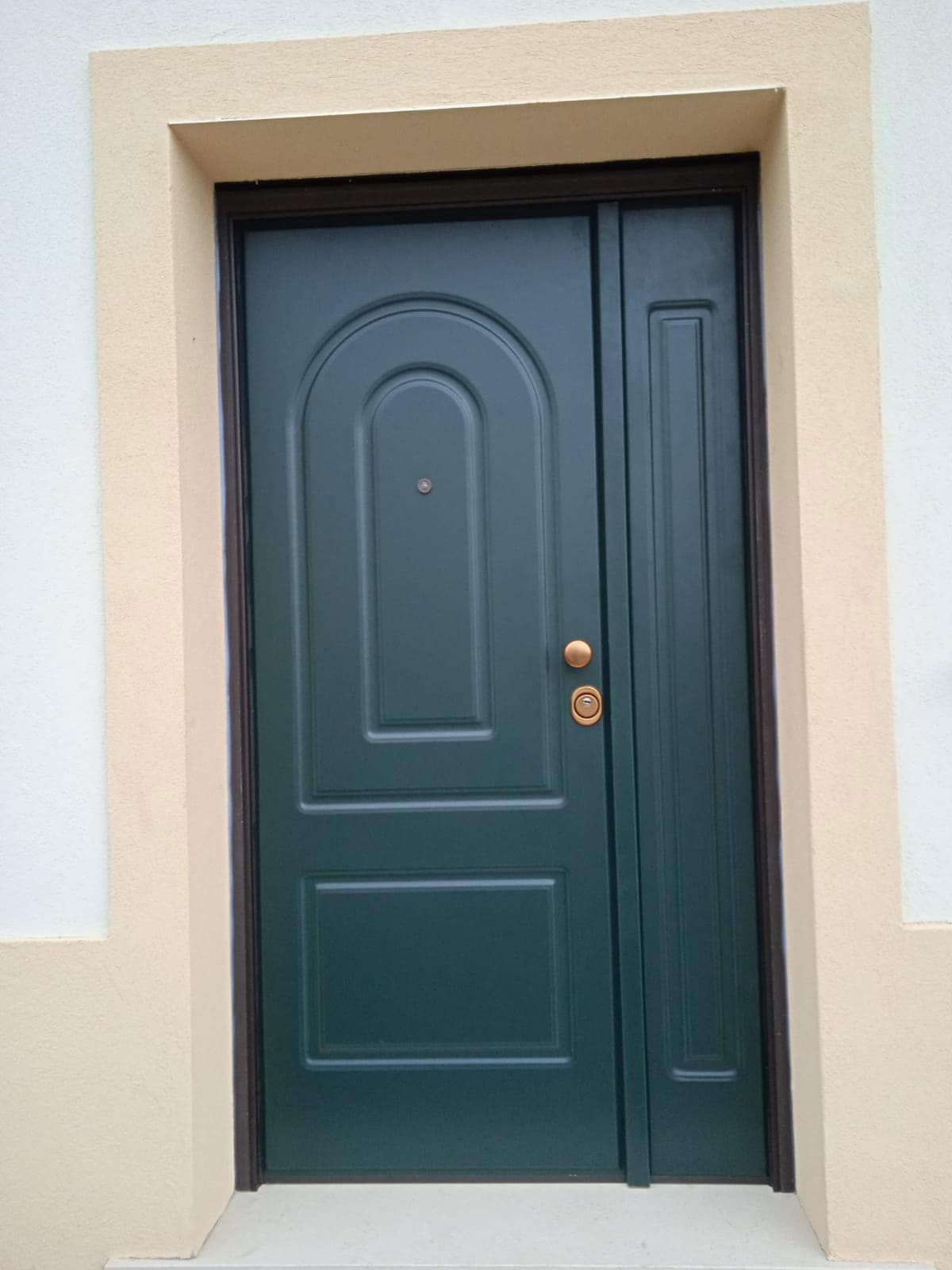 Una porta verde con una maniglia dorata si trova su una parete marrone chiaro