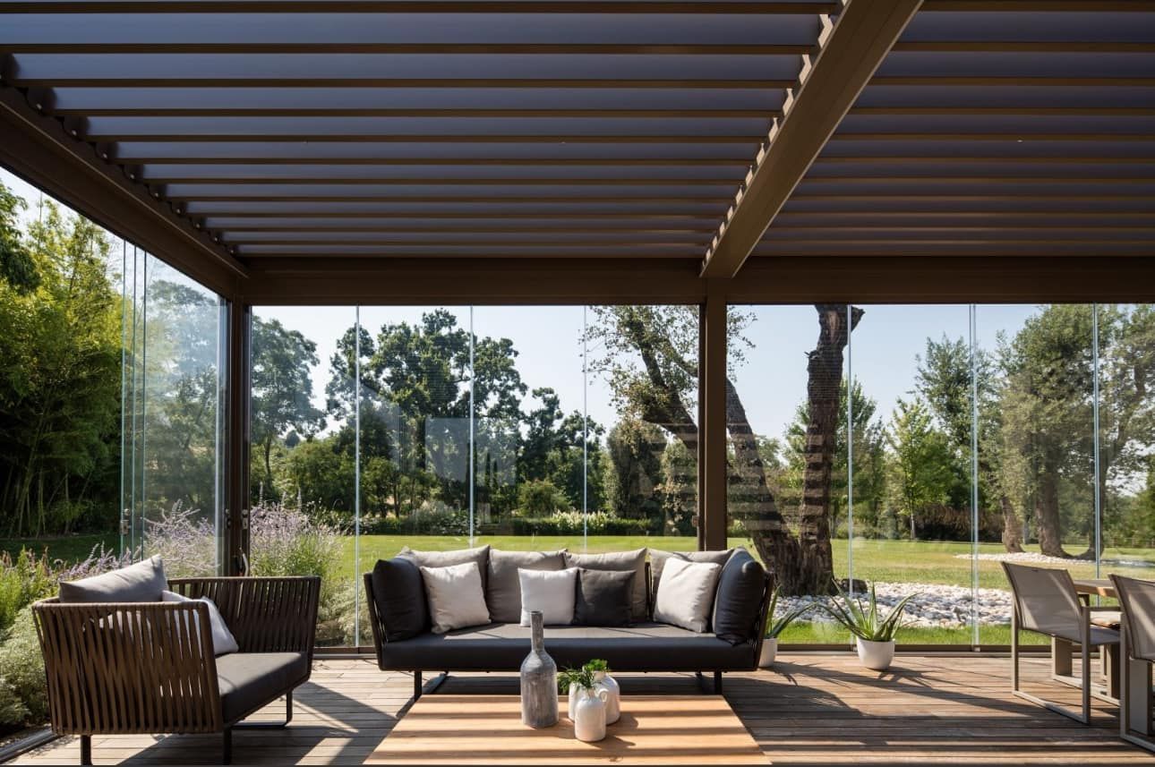 Un soggiorno con divano, sedie e tavolo sotto un pergolato.