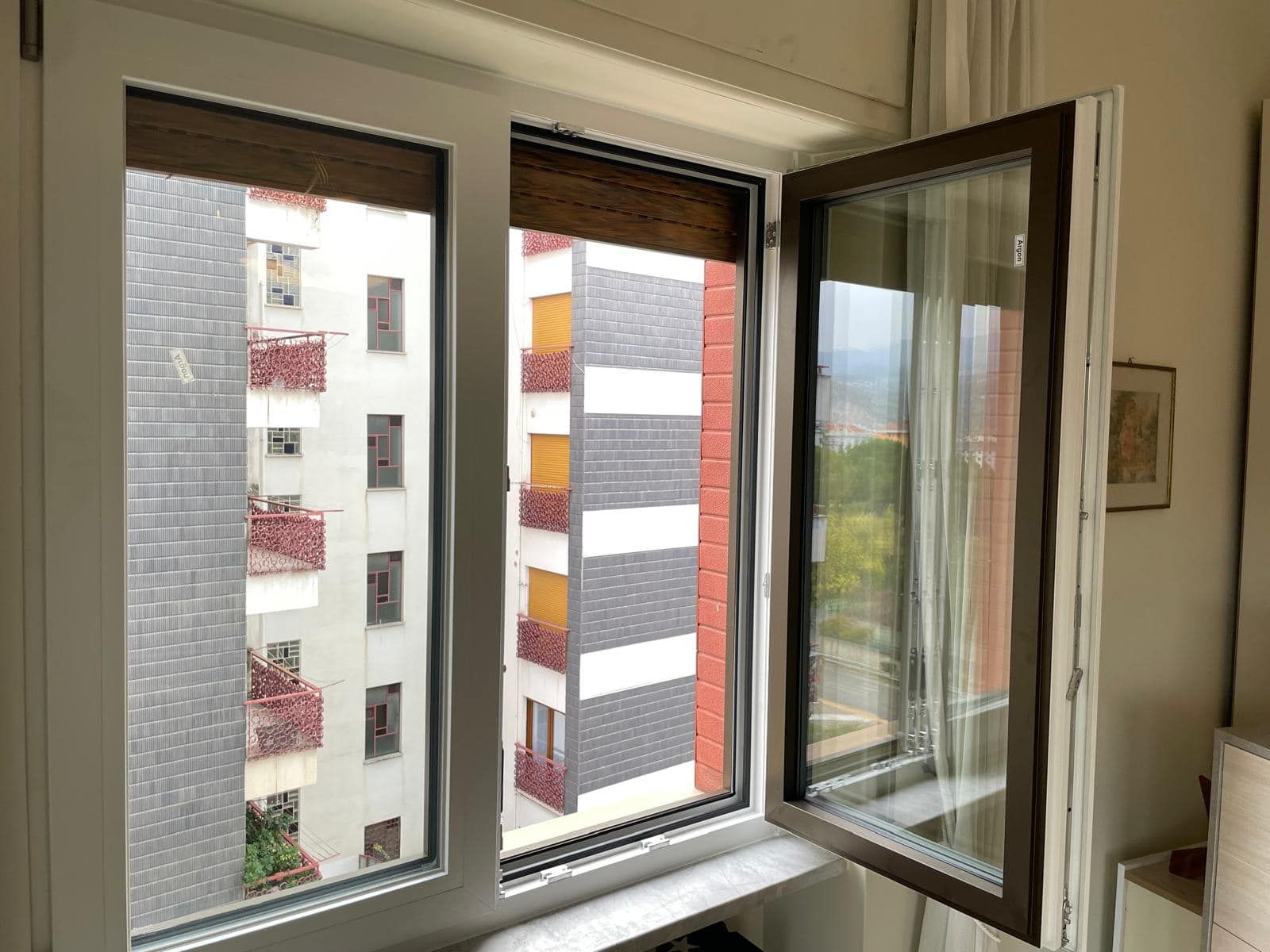 Una stanza con due finestre aperte e vista su un edificio.