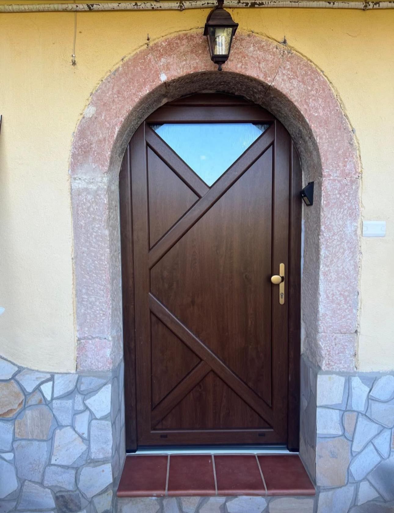 Una porta di legno con un arco di pietra e una lampada sopra