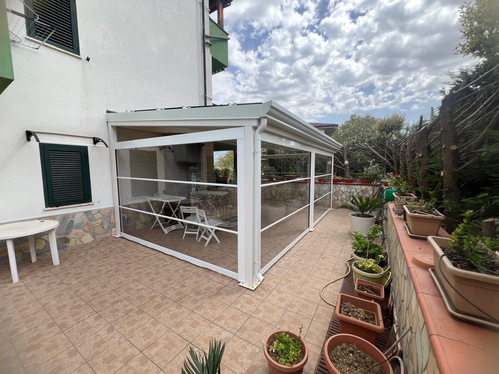 Un patio con tavolo, sedie e piante in vaso di fronte a una casa.