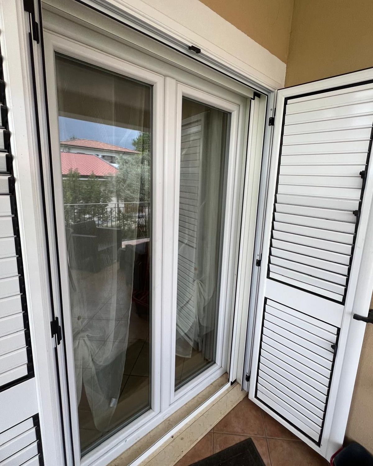 Una porta bianca con persiane nere è aperta su un balcone.