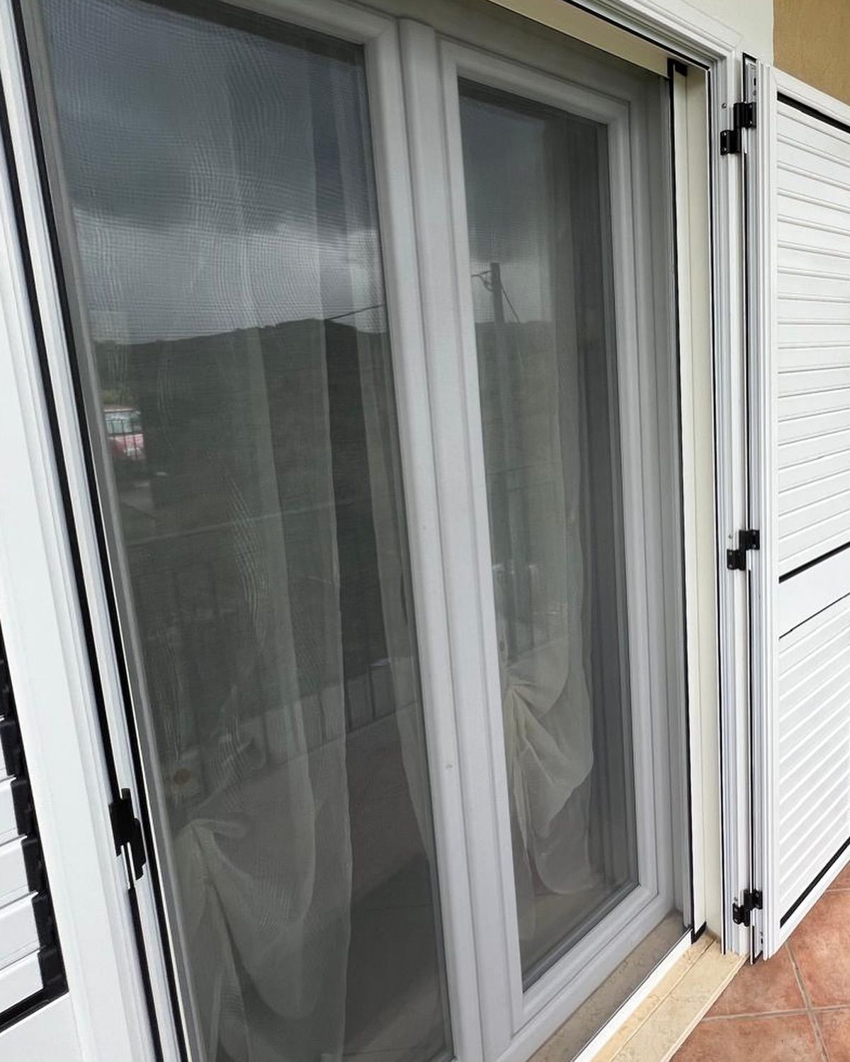 Primo piano di una porta scorrevole in vetro con persiane bianche.