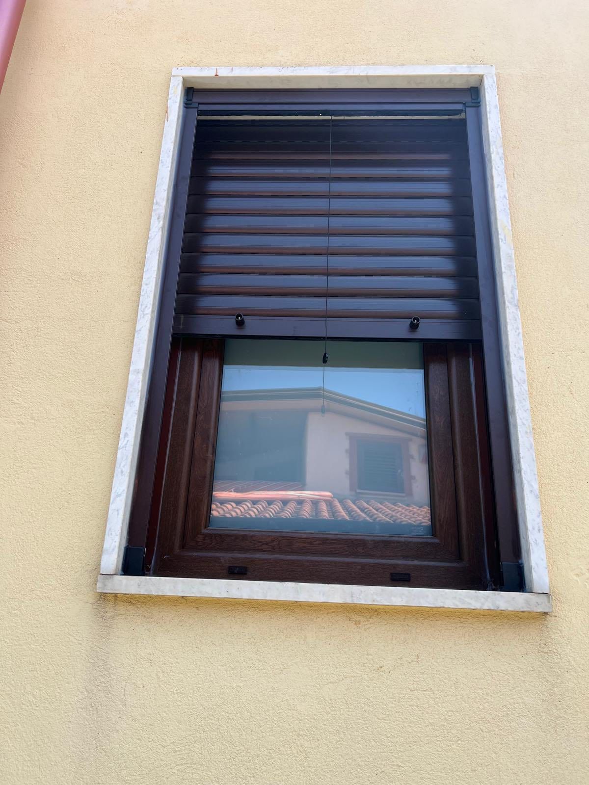 Una finestra con una persiana si trova su un muro giallo.