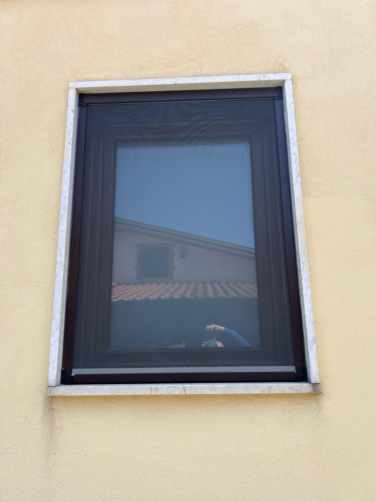 Una finestra con una zanzariera si trova su una parete gialla.