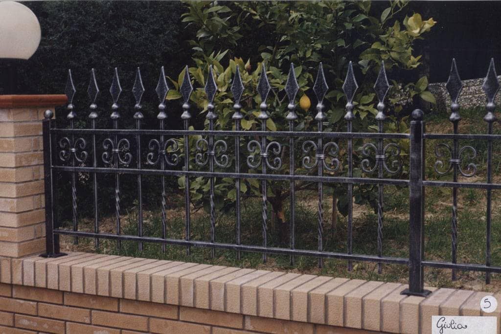 Una recinzione in ferro battuto circonda un muro di mattoni