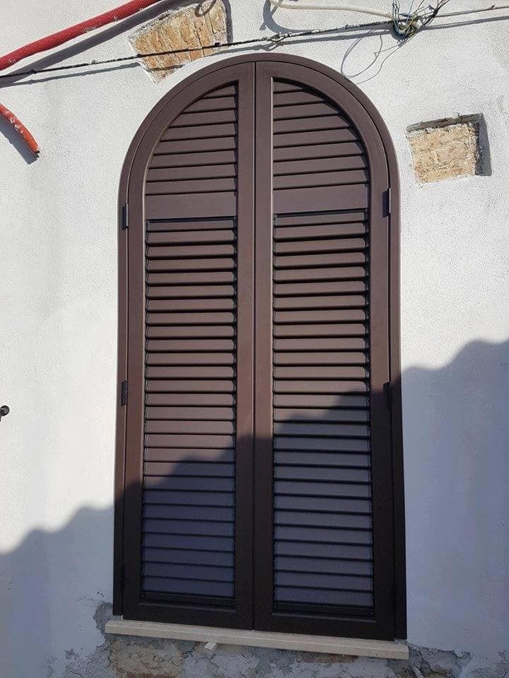 Una finestra con persiane ad arco su un muro bianco