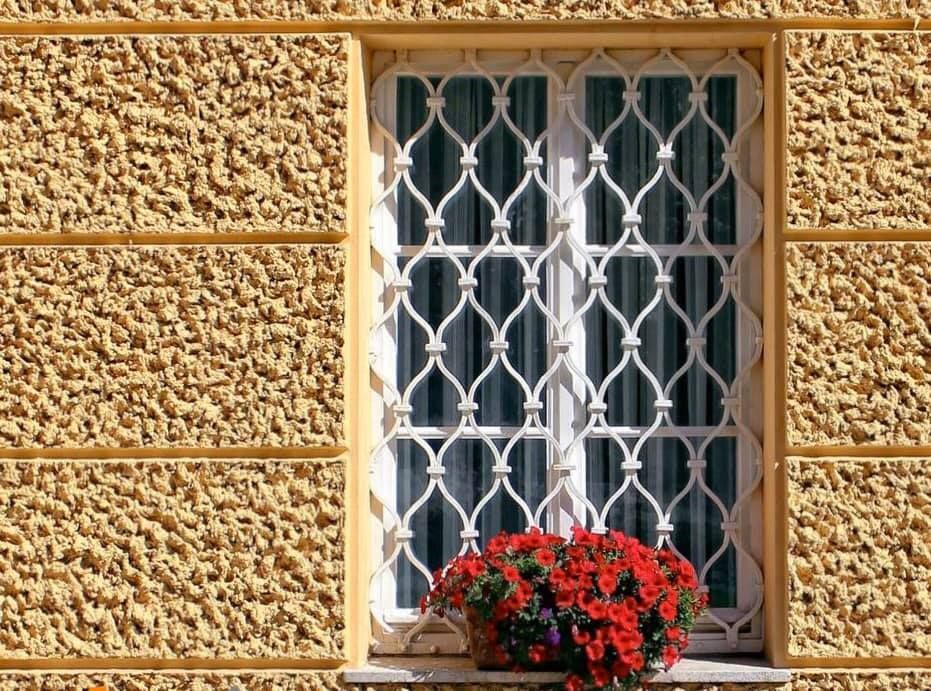 Una finestra con una grata in ferro battuto e fiori sul davanzale.