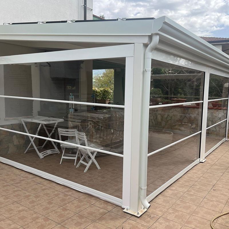 Un pergolato bianco con pareti in vetro trasparente, tavoli e sedie.