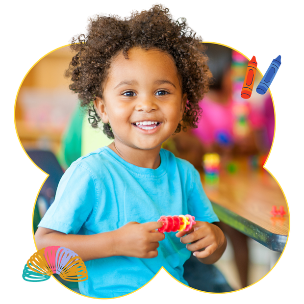 Smiling child holding a toy, in a brightly lit setting, with crayons and slinky.