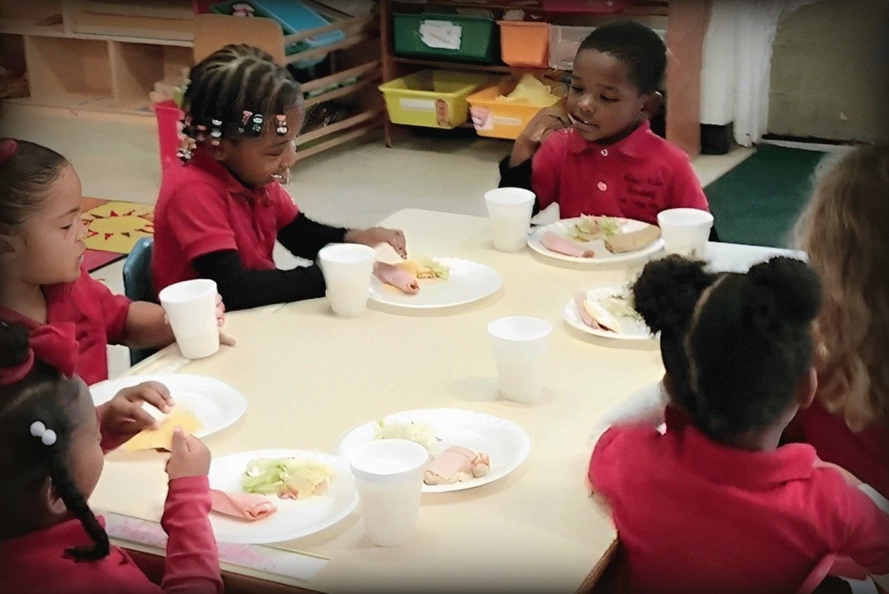 Children in red shirts eating at a table in a classroom.