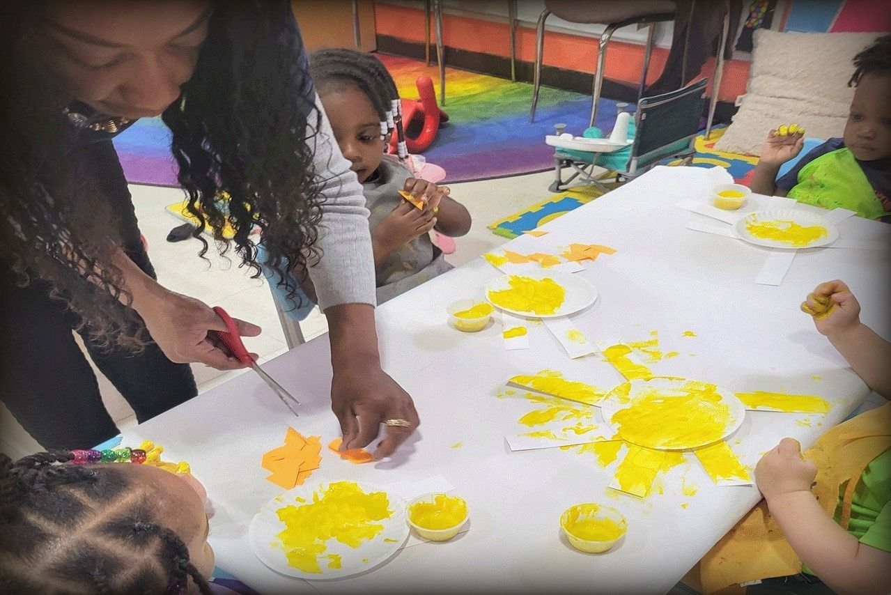 Teacher and children do art project at a table with yellow paint.