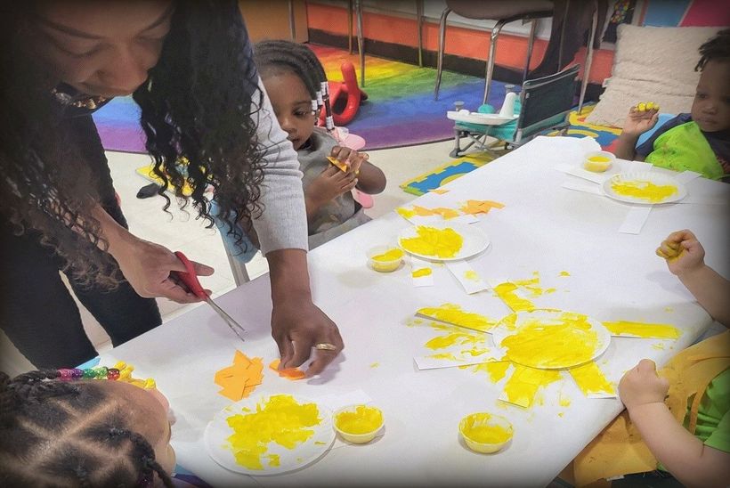 Teacher and children do art project at a table with yellow paint.