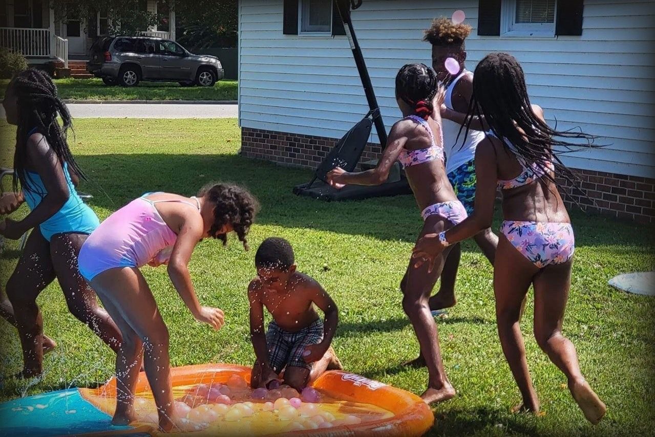Children playing in a small pool on a sunny lawn, splashing water and laughing.