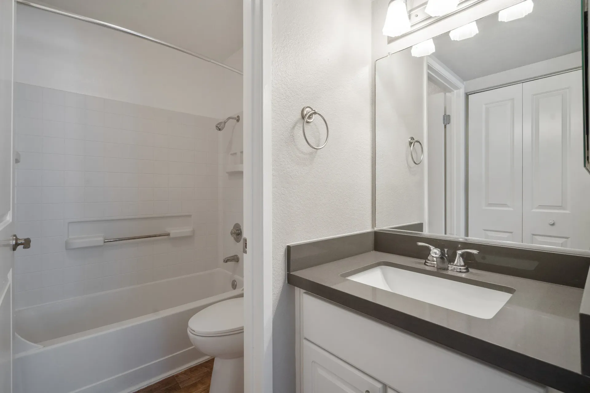 Bathroom with tub/shower combo, grab bar, toilet, and vanity with sink.