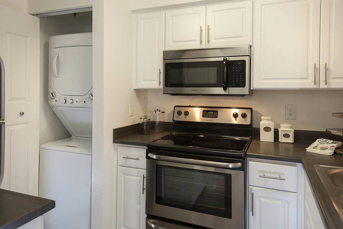 Kitchen with stainless steel stove and microwave, white cabinets, and a stacked washer/dryer in a closet.